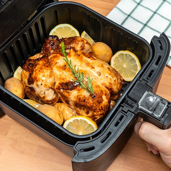 Roast chicken and potatoes in a cooking pan, garnished with lemon and rosemary
