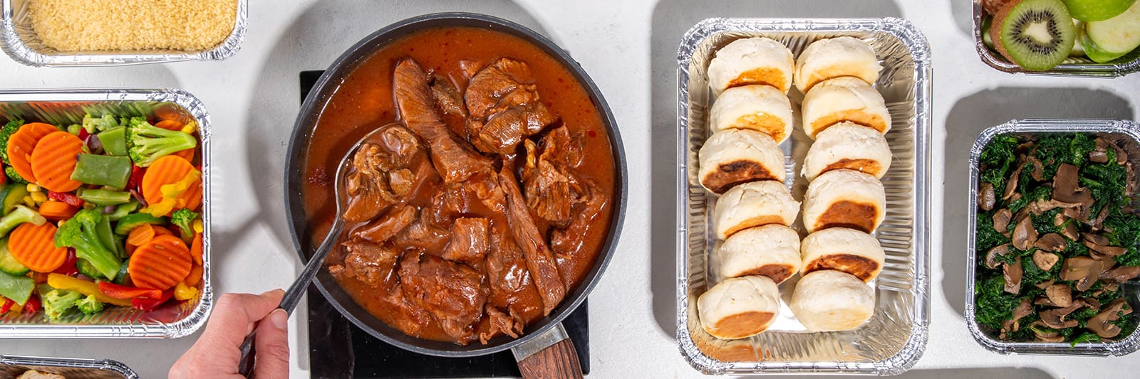 Assorted meals including stewed meat, steamed vegetables, bread rolls, and sautéed greens in containers