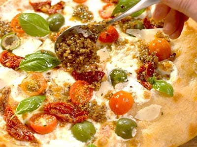 Spoon garnishing pesto onto a freshly baked pizza with tomatoes and basil