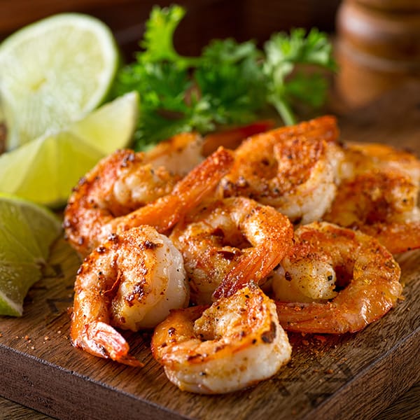 Grilled shrimp seasoned with spices on a wooden board, garnished with lime and herbs