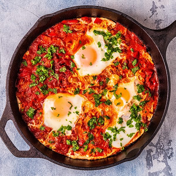 Shakshuka with eggs poached in a tomato and pepper sauce, garnished with herbs in a skillet