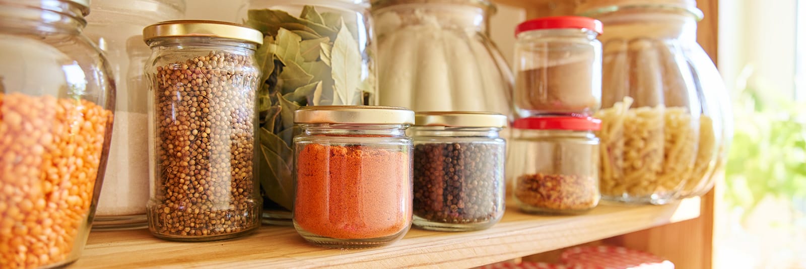 Variety of grains and spices in glass jars on a kitchen shelf
