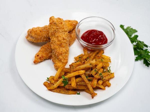 Plate with crispy chicken tenders, seasoned fries, and a side of ketchup
