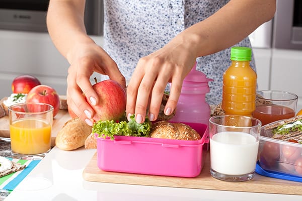 Person packing a healthy lunch with a variety of foods and drinks on a kitchen counter