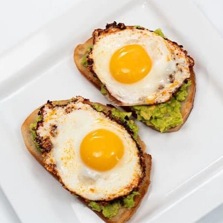 Avocado toast with sunny-side-up eggs served on a white plate