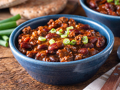 Bowl of chili garnished with green onions, served with bread on wooden table