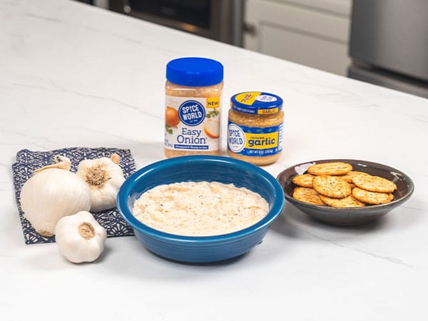 A bowl of dip with garlic and crackers, accompanied by spice jars