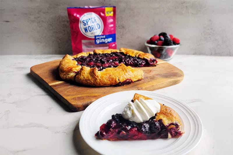Sliced homemade berry galette with a dollop of whipped cream on a plate, packaged ginger in the background