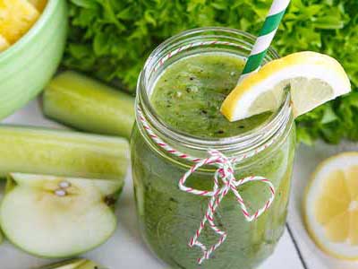 Green smoothie in a jar with a lemon slice and striped straw, suggesting healthy eating