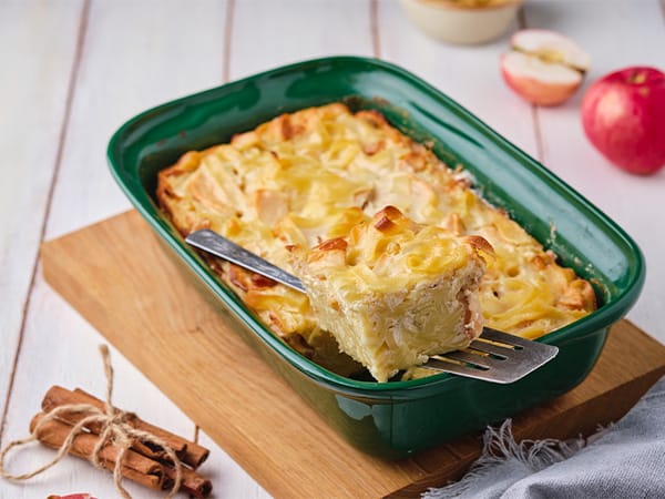 Apple and cheese bake served in a green dish, a piece lifted on a spatula