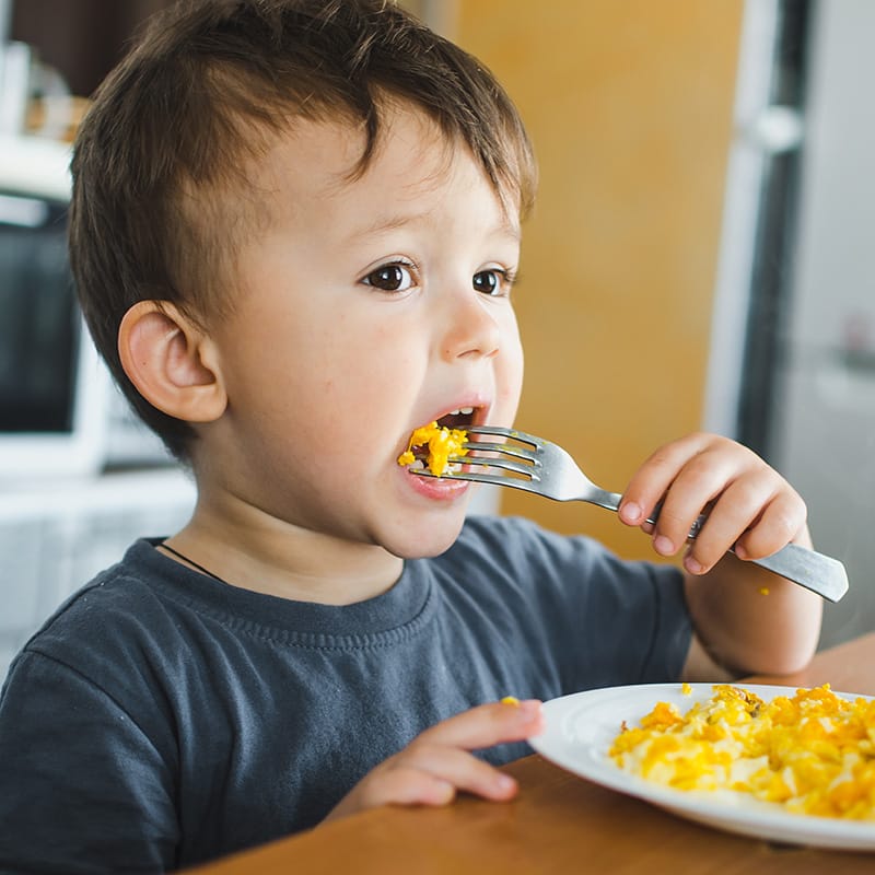 Young boy eating scrambled eggs with a fork at the table, enjoying his meal.