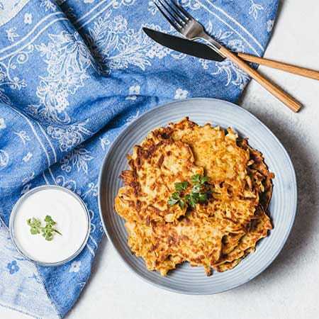 Plate of latkes served with sour cream on a blue patterned cloth