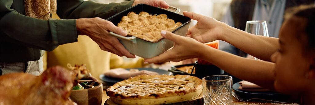 Family hands serving dessert at a festive gathering with various dishes on the table