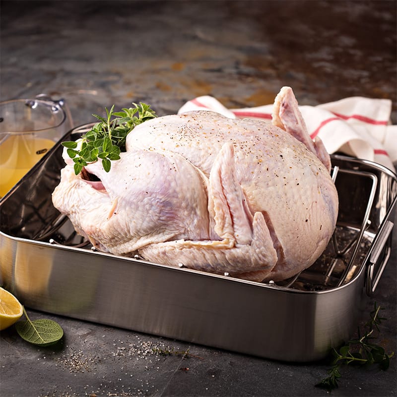 Raw turkey in a roasting pan, garnished with herbs, ready for preparation for a delicious meal