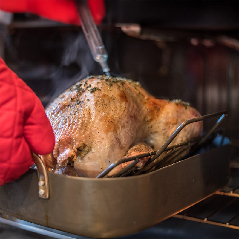 A person prepares a roasted turkey in the oven, highlighting cooking techniques for a delicious meal
