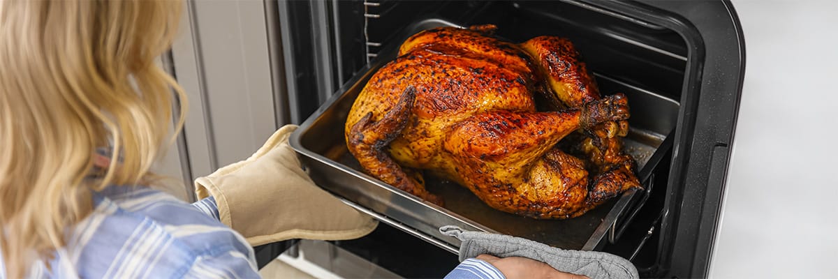 A person carefully removing a roasted chicken from the oven, showcasing a delicious home-cooked meal