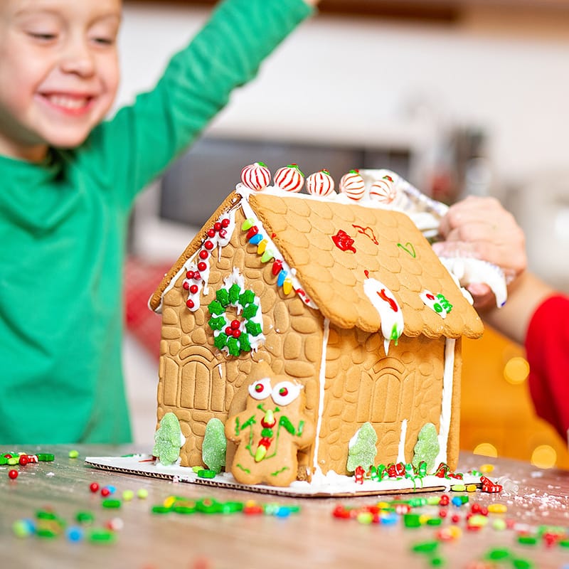 Children joyfully decorating a gingerbread house with colorful candies and icing during a festive activity