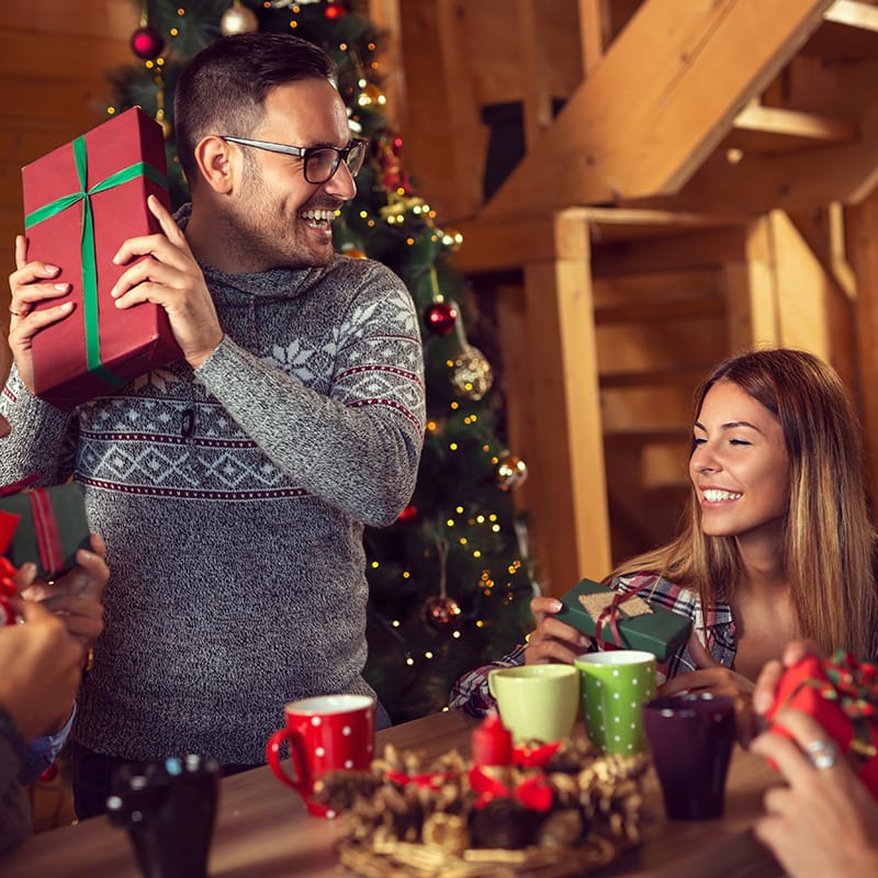 Friends celebrate with gifts and festive drinks around a cozy holiday setting