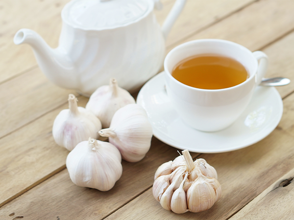Cup of tea beside garlic heads and a teapot on a wooden table, highlighting unique flavor combinations