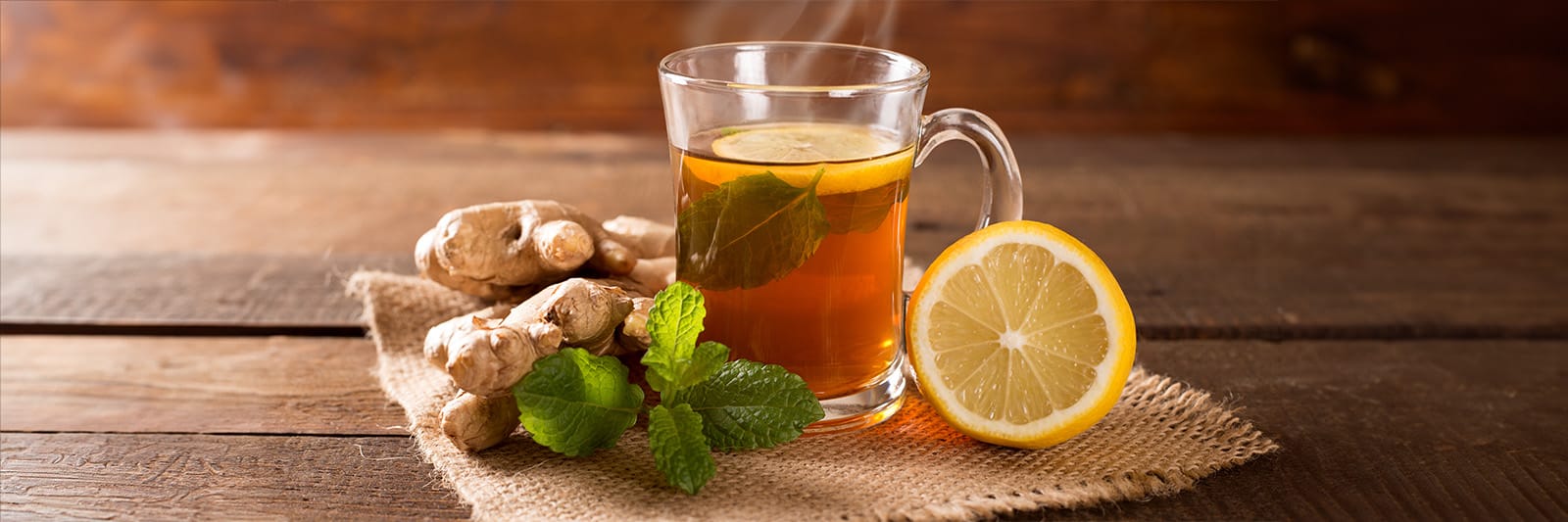 Warm ginger tea with lemon and mint leaves on a rustic table, highlighting a cozy beverage experience