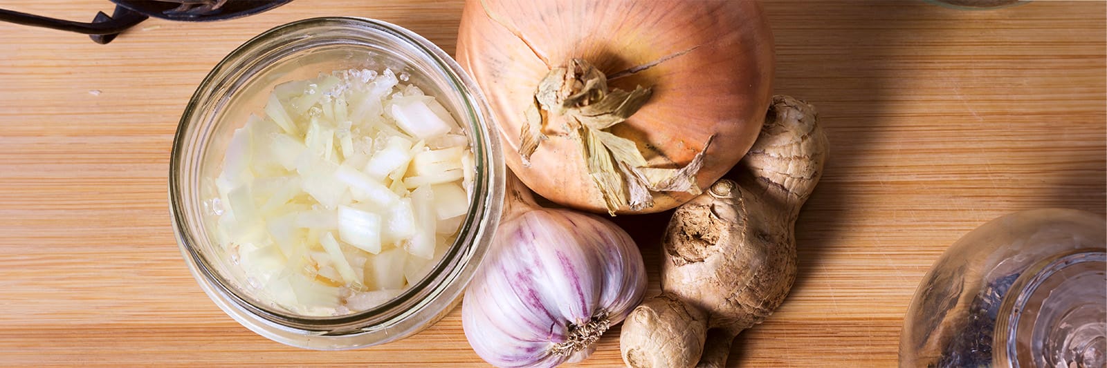 Chopped onions and garlic in a jar, surrounded by fresh ginger and onions on a wooden surface, ready for cooking