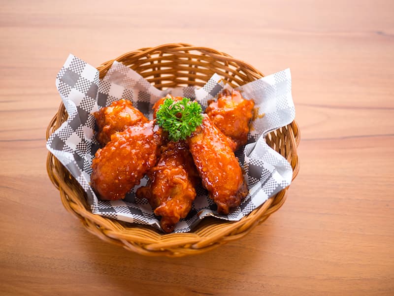 Basket of glazed chicken wings garnished with parsley, perfect for sharing during a meal or gathering