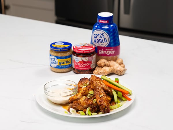 Plate of chicken wings with dipping sauce, surrounded by spices and fresh ingredients for a flavorful meal