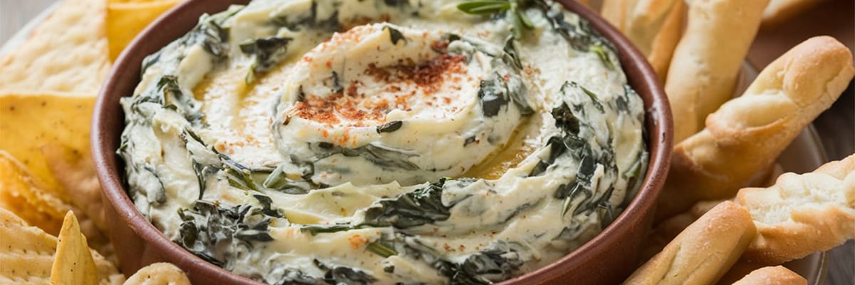 Creamy spinach dip served in a bowl with assorted crispy crackers and breadsticks for sharing