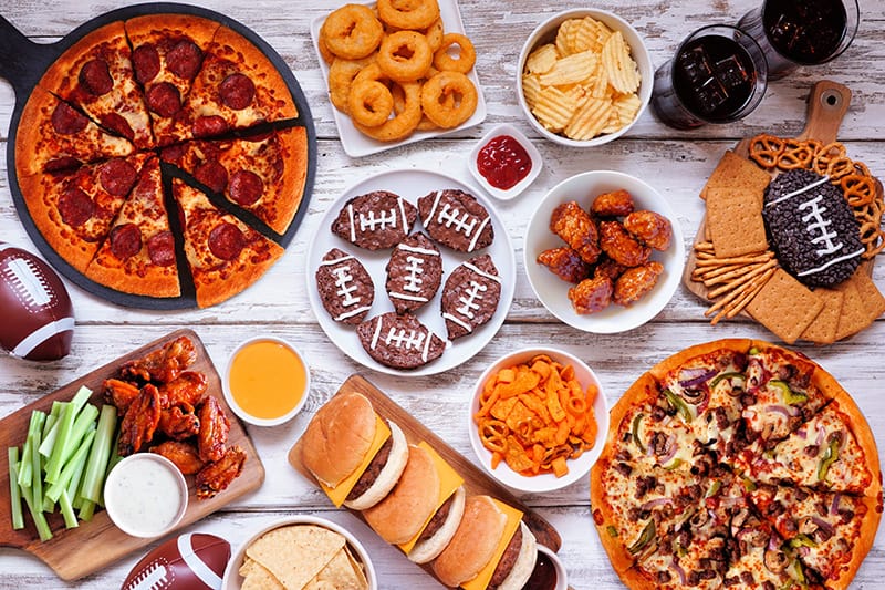 A festive spread of appetizers and snacks ideal for game day, featuring pizza, wings, cookies, and chips
