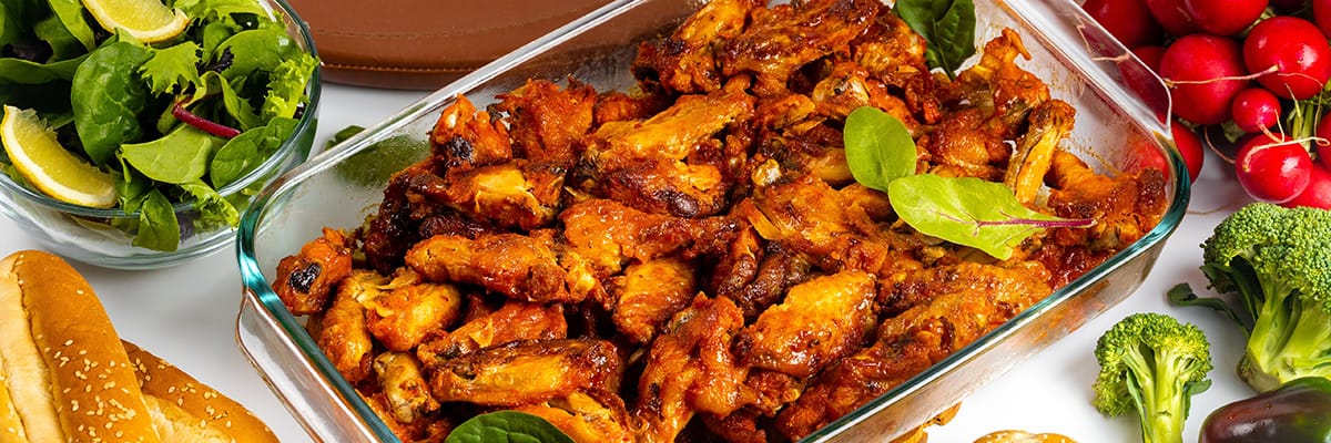 Baked chicken wings served with a fresh salad, hot dog, and mixed vegetables, perfect for a delicious meal