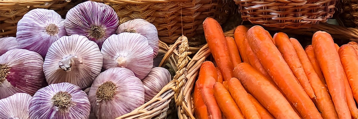 Baskets of fresh garlic and carrots, showcasing vibrant vegetables for cooking and meal preparation
