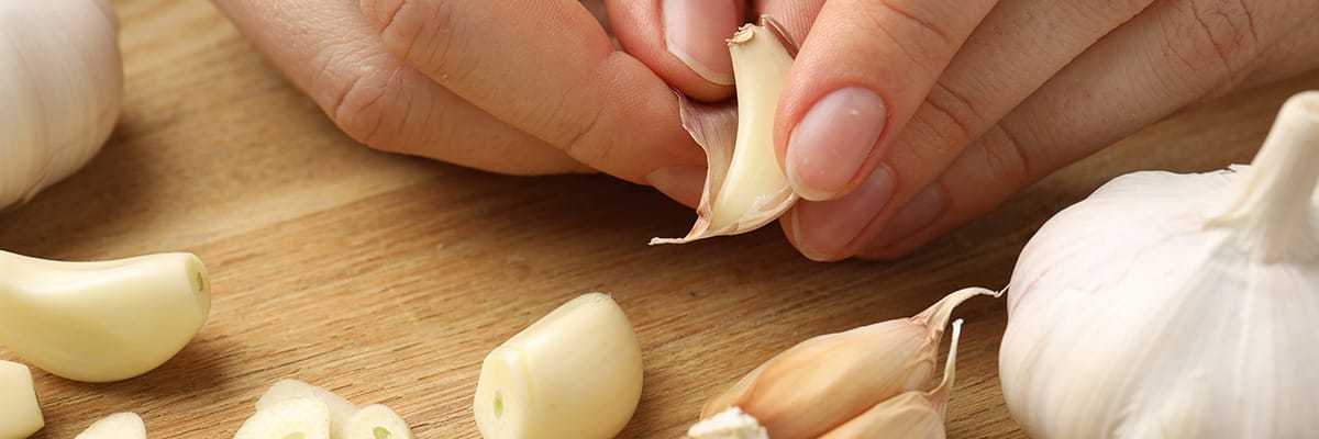 A person peeling garlic cloves on a wooden countertop for cooking delicious meals