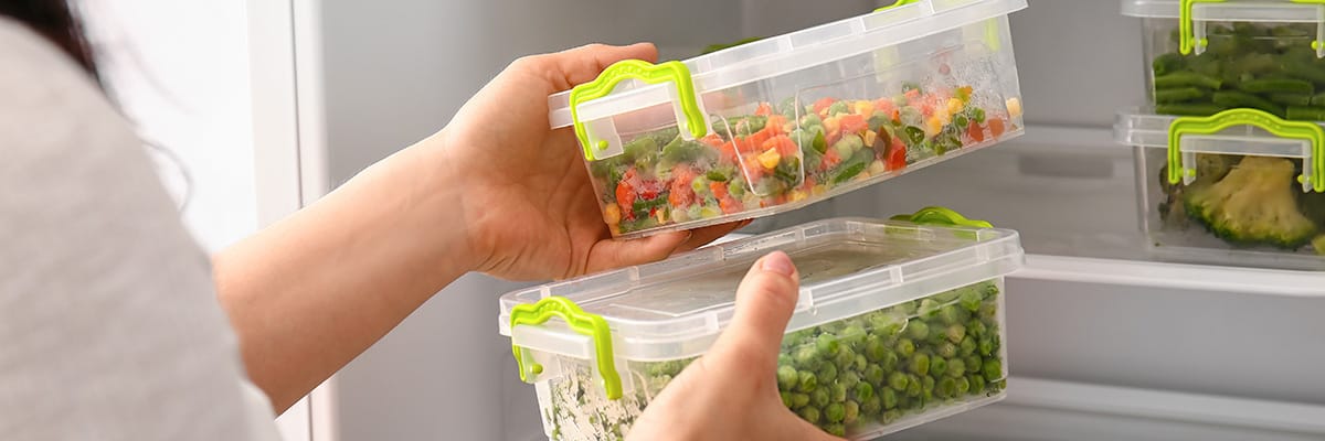 Hands placing fresh meal prep containers into a refrigerator for storage and organization of healthy food
