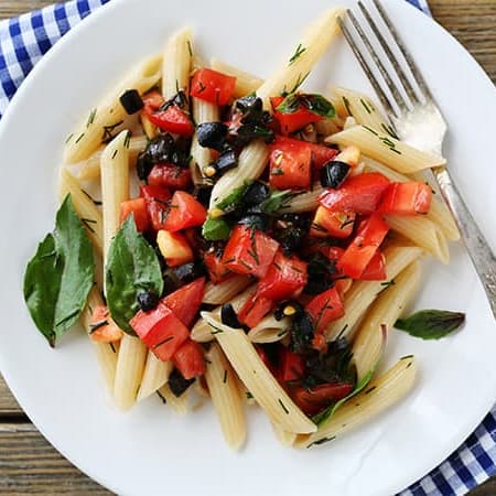 Plate of pasta topped with fresh tomatoes, olives, and herbs, served with a fork, on a checkered napkin