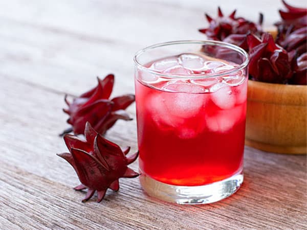 Refreshing hibiscus drink served over ice, with dried hibiscus flowers in the background. Perfect for a warm day
