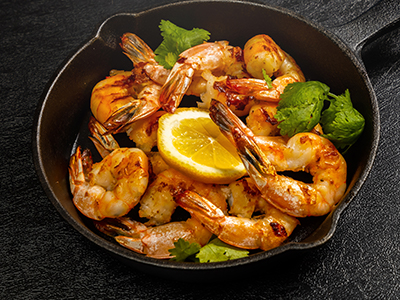 Grilled shrimp served in a skillet with fresh herbs and a lemon slice, perfect for a delicious meal