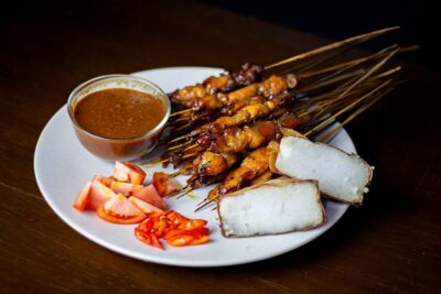 Plate of skewered grilled meat with spicy sauce, accompanied by fresh vegetables and rice cakes, showcasing a delicious meal