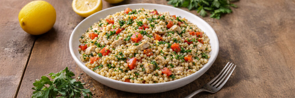 Couscous salad with chicken, tomatoes, and herbs, served with lemon on a wooden table. Perfect for a fresh meal