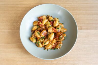 Plate of gnocchi topped with sun-dried tomatoes and herbs, showcasing a delicious meal