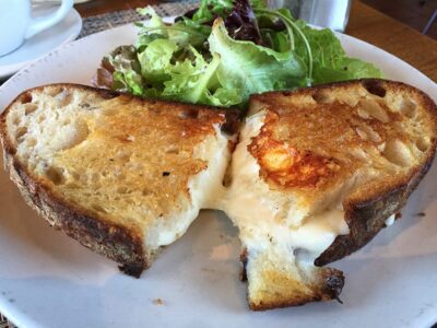 Grilled cheese sandwich cut in half, served with a side of fresh mixed greens on a plate