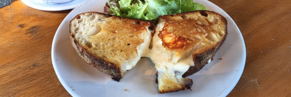 Grilled cheese sandwich with melted cheese and a side of fresh greens on a white plate