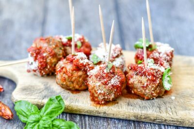 Delicious meatballs topped with sauce and herbs, served as an appetizer on a wooden tray