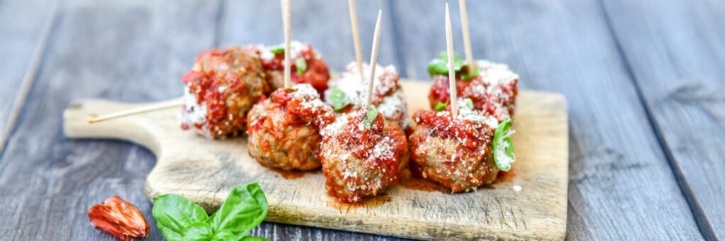 Delicious meatballs topped with sauce and herbs, served on a wooden board, perfect for a hearty meal or appetizer