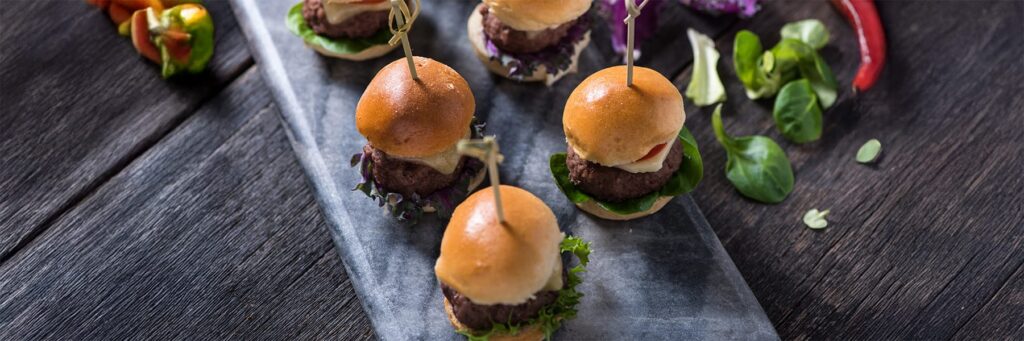 Mini burgers displayed on a platter, garnished with greens, perfect for a gourmet tasting or gathering