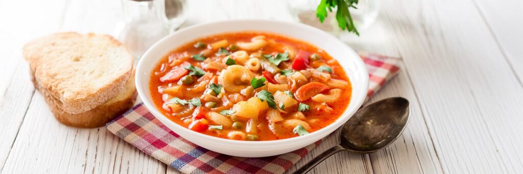 A warm bowl of pasta soup with vegetables and bread, perfect for a comforting meal