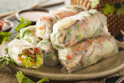 Fresh summer rolls filled with vegetables, served on a plate with dipping sauces
