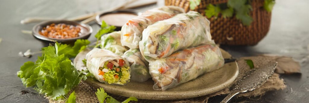 Fresh summer rolls filled with vegetables, served on a plate with dipping sauces