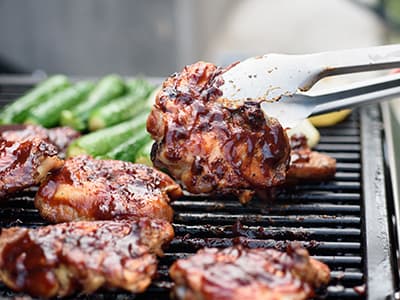 Grilled chicken thighs being lifted from the barbecue, alongside grilled vegetables, ready to be served