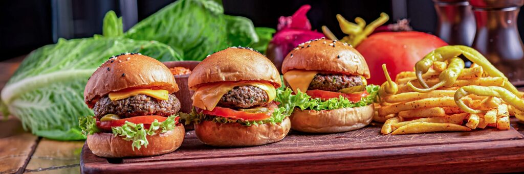 Three delicious burgers accompanied by fries and fresh vegetables, showcasing a tempting meal setup