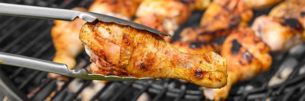 Grilled chicken drumstick being lifted with tongs, highlighting delicious barbecue food